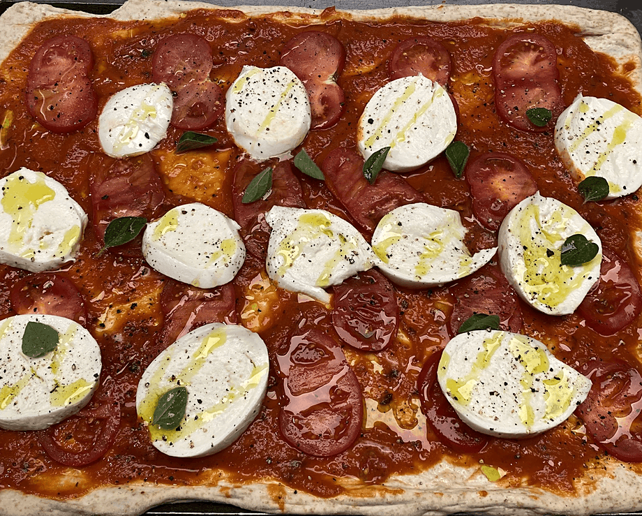 Assembled raw pizza with mozzarella and fresh tomato on a tomato sauce base